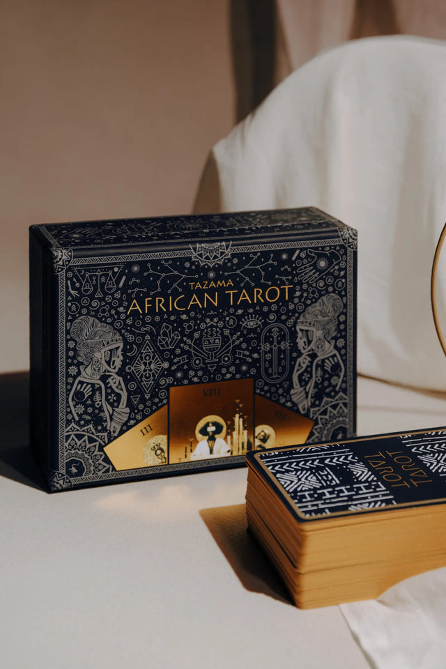 The Tazama African Tarot deck box with the stacked tarot cards that have gold gilding sitting in front of it.