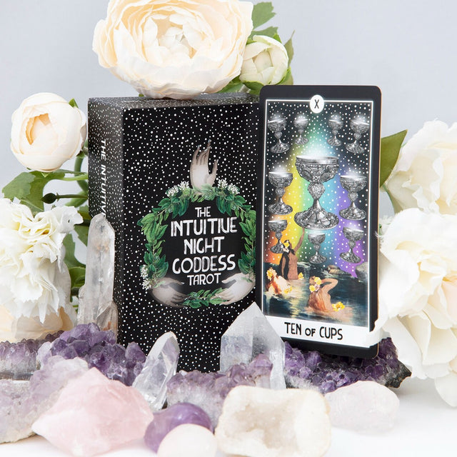The Intuitive Night Goddess tarot deck box with one card, the Ten of Cups, to the side, and white roses and amethyst crystals around them