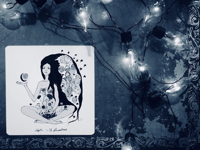 A tarot card of a woman, the Priestess, sitting next to a table with lights on it