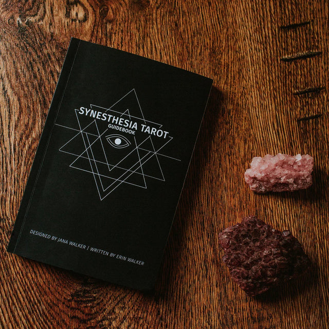 The Synesthesia Tarot guidebook on a wooden table next to two crystals