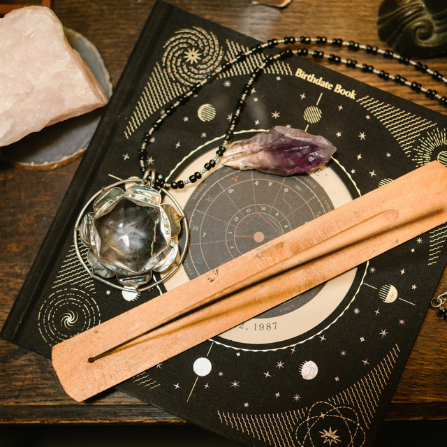 A black and gold astrology book with a pendant, crystal, and incense holder on top of it