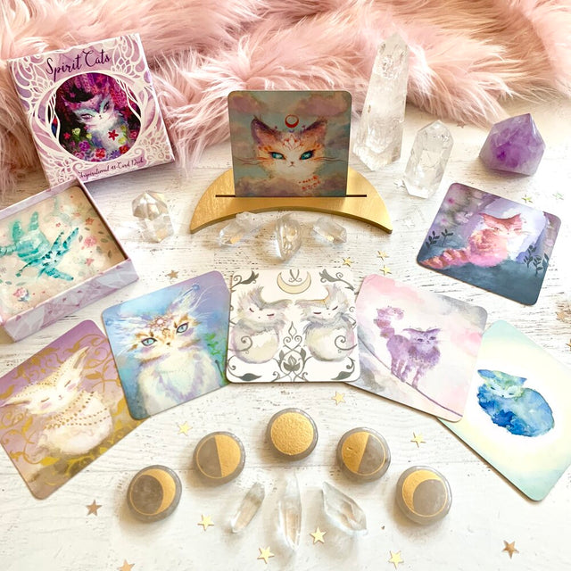 A selection of oracle cards from the Spirit Cats Oracle Deck with clear crystals, star decorations, and a furry pink blanket in the background.