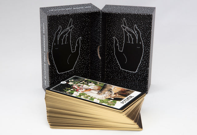 The inside of the Intuitive Night Goddess deck box showing two hands in a starry background, with the gold-gilded cards stacked in front